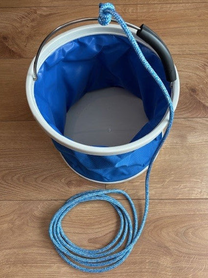 Angled overhead view of the open blue folding bucket showing its grey base, black handle grip and attached blue lanyard.